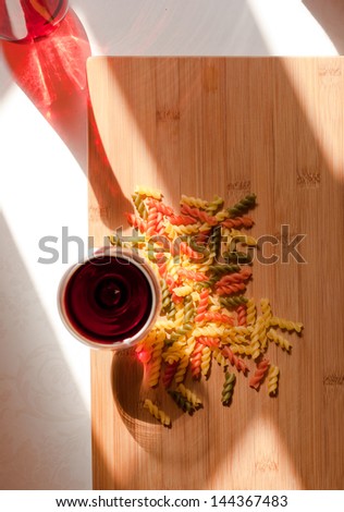 Still life with colorful pasta and glass of red wine and colorful bottle in natural lighting.