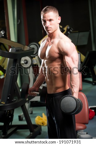 Portrait of a handsome young man doing arm exercises in a gym.