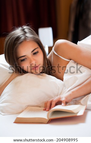 Beautiful young brunette reading a book before going to sleep.