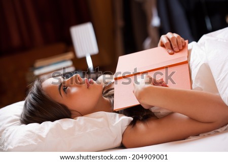Gorgeous young brunette woman immersed in reading a book in bed.