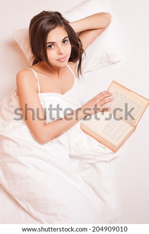 Gorgeous young brunette woman immersed in reading a book in bed.