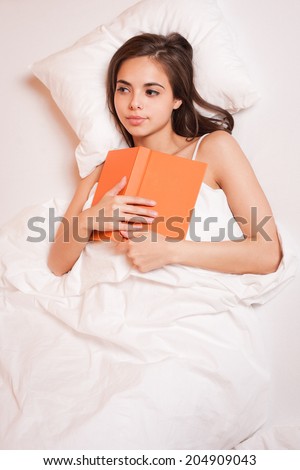 Beautiful young brunette reading a book before going to sleep.