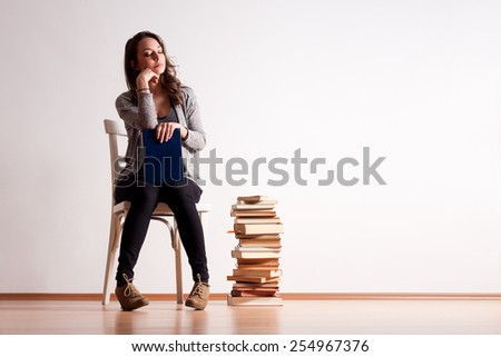 Gorgeous young brunette student woman next to column of books.