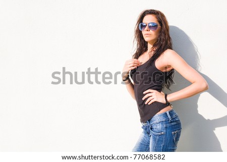Hot summer sunlight on hot young brunette girl in front of white wall wearing sunglasses.