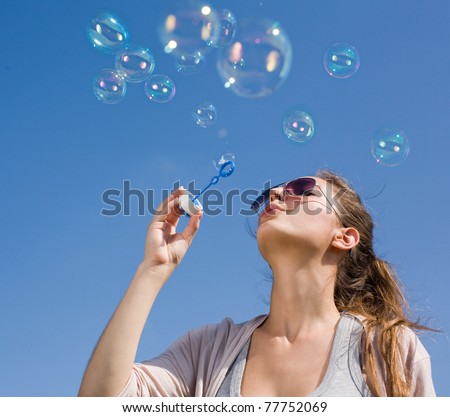 Beautiful young brunette girl blowing soap bubbles into the sky.