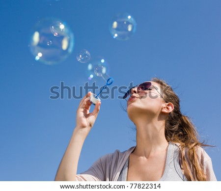 Gorgeous young brunette blowing soap bubbles into the sky.