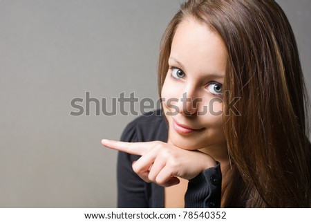 Beautiful smiling young  brunette girl pointing towards left with her index finger.