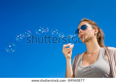 Beautiful young brunette girl blowing a wave of soap bubble to the clear blue sky.