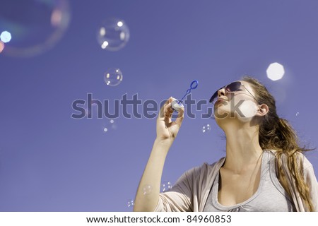 Gorgeous young brunette girl blowing soap bubbles in front of clear blue sky.