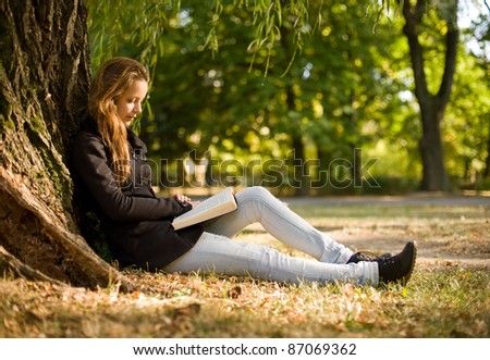 Portrait of beautiful young brunette girl reading a book in the park at fall.