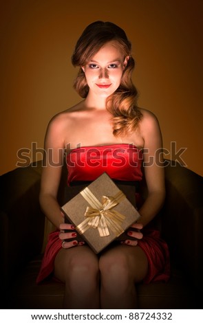 Portrait of beautiful smiling relaxed young blond with magical gift box in creative lighting.
