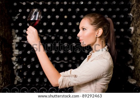 Beautiful young brunette woman tasting wine, checking the color in the wine cellar.