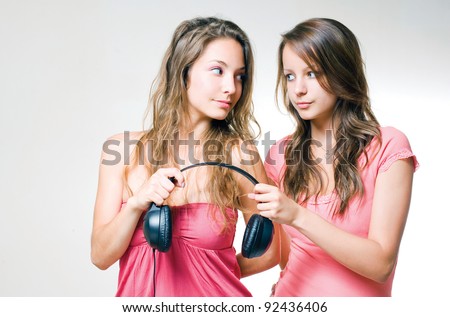 Music sharing concept two beautiful young brunette teens holding on to a headphone, one with worried expression.