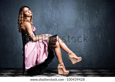 young  blond woman in elegant pink dress sit on chair in empty grunge room with tiled floor