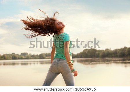 curly hair young woman jump in front of lake  summer day casual clothes