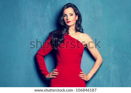 beautiful elegant woman in red dress  with one sleeve on blue wall studio shot