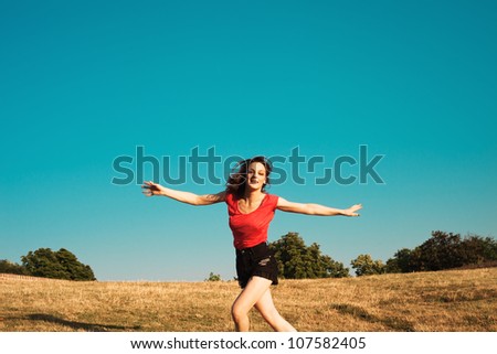 smiling girl in shorts and t-shirt run with open arms on the hill,  summer hot day, blue sky in background and dry grass