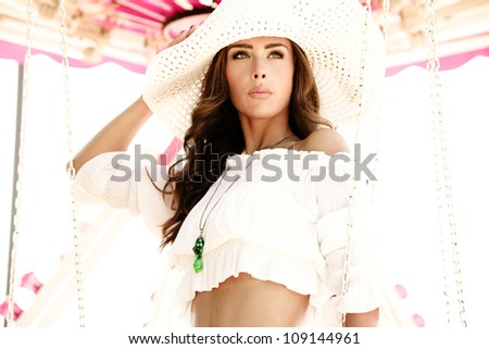 fashion girl in summer outfit and hat pose at carousel in amusement park