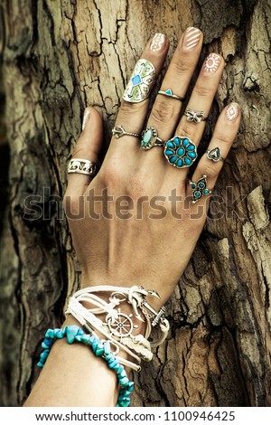 closeup of woman hand on tree surface  with lot of boho style jewrly, rings and bracelets outdoor summer day
