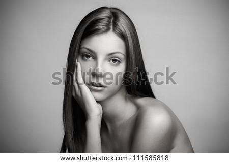 natural beauty portrait of a young woman with long straight hair with hand on chin in black and white studio shot small amount of grain added