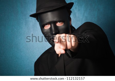 man with black mask and hat point with finger towards camera