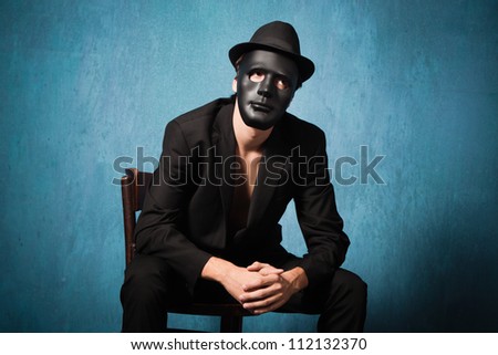 scary man in black suite with black mask and hat sit on chair