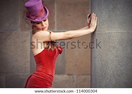 young elegant woman in red dress and cylinder  leaning against column