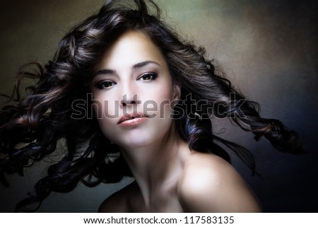 sensual brunette woman with shiny curly silky hair in motion studio shot