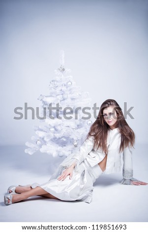 smiling beautiful brunette woman in silver dress sit by the christmas tree