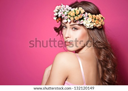 beautiful brunette young woman with wreath of flowers studio shot pink background