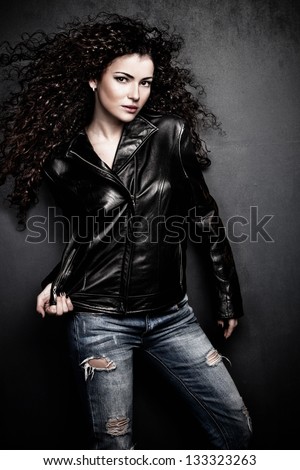 attractive long hair young woman in black leather jacket and blue jeans studio shot small amount of grain added