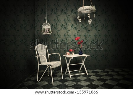old room with floral wallpaper, tiled floor, chair and table, cup of tea vase with flowers and birdcage full of flowers