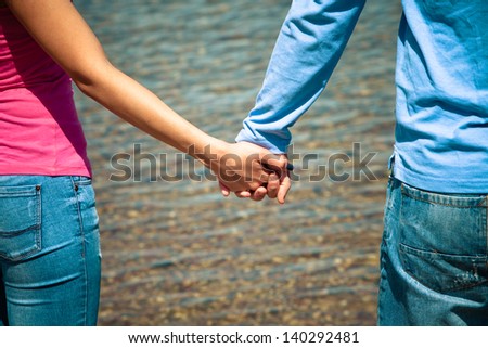 couple standing in front water with hand in hand
