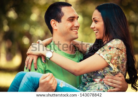 smiling young man carrying her girlfriend in arms outdoor shot in park summer day
