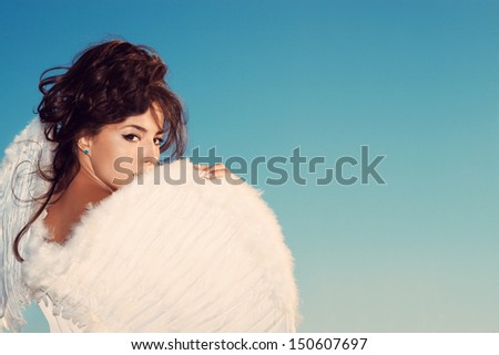 beautiful young brunette woman  with angel wings against blue sky,  outdoor shot, small amount of grain added