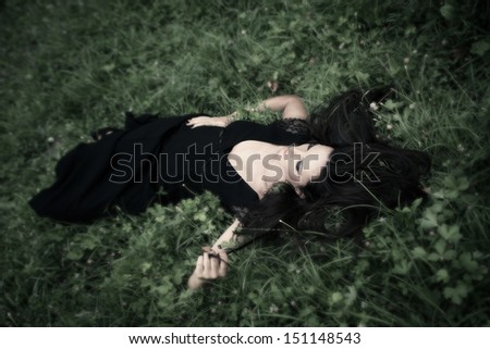 elegant  woman in long black dress lie in grass  full body shot