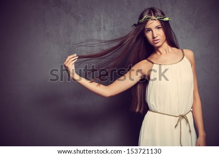 natural looking young woman with long straight hair in white simply  dress  and wreath of leaves in hair studio shot