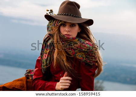 young blond woman in autumn fashion clothes,  red leather jacket, hat, cashmere scarf and brown skirt outdoor shot