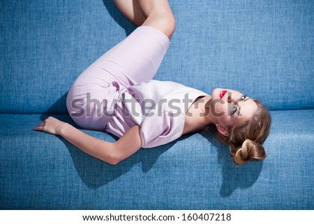 beautiful blond woman in classic elegant pink dress lie on blue sofa indoor shot