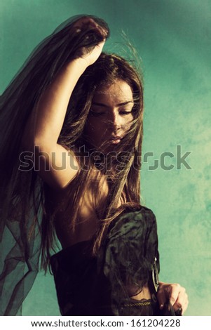 beautiful young woman with black veil in one hand, hair flying across her face, eyes closed, green wall behind her