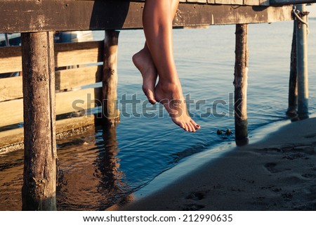 woman legs as she sitting on old wooden dock at sea shore