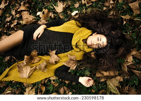beautiful woman with eyes closed  lie in grass and autumn leaves wearing dark green dress and long yellow wool scarf