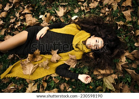 beautiful woman  lie in grass and autumn leaves wearing dark green dress and long yellow wool scarf