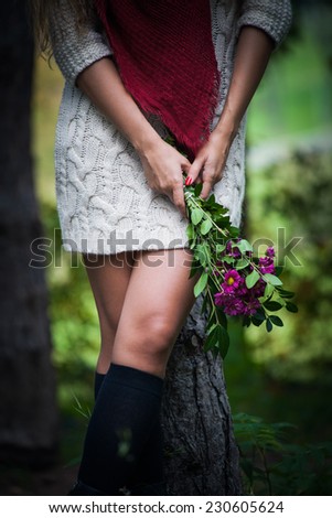 autumn fashion details, woman hands hold flowers, wool dress, red scarf, legs in black leggings outdoor shot in forest