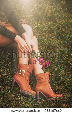 woman legs in brown ankle high heel boots sit on grass hold flowers in hands