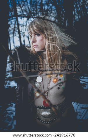 blonde woman in coat and wool dress in hippie style apperel stand alone in wood, cold winter day