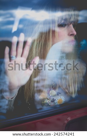 young woman portrait in the car behind the window, hand on glass looking away