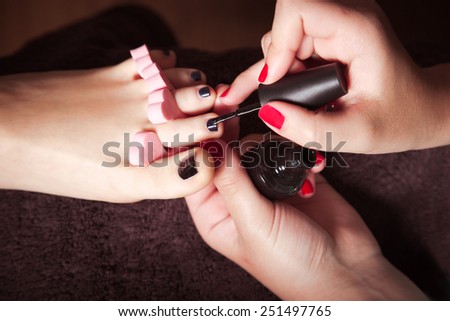 woman at cosmetics salon applying black  nail polish on toenails