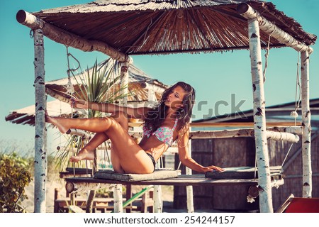 young woman in bikini  sit at shade at seaside beach enjoy in summer hot sunny day, full body shot