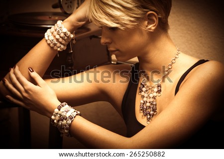 short hair blond elegant young woman portrait wearing jewelry, necklace and lot of bracelets, indoor shot, side view